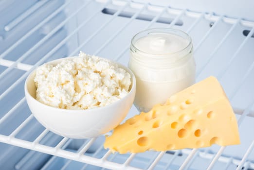 tasty and healthy dairy products on the shelf in the refrigerator: sour cream in the bank, cottage cheese in  bowl and slab of cheese 