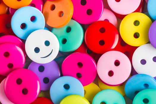 bright multicolored buttons of red, yellow, blue, orange, pink color, among them the white button - smiley stands out among other, top view