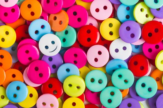 bright multicolored buttons of red, yellow, blue, orange, pink, purple, color, among them the white button - smiley stands out among other, top view