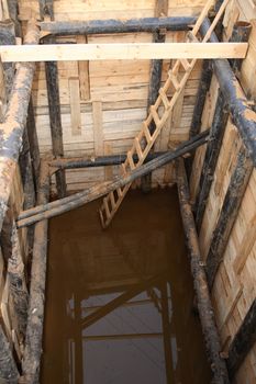 Pipeline mending. Deep pit in land with wooden ladder and pipes