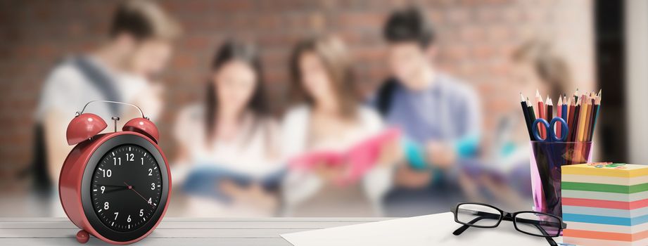 School supplies on desk against happy students standing and reading