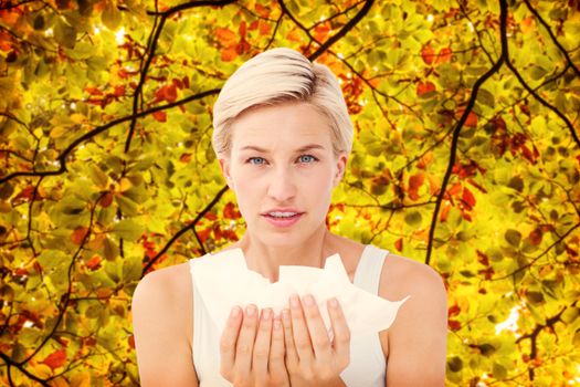 Sick woman holding tissues looking at camera  against branches and leaves