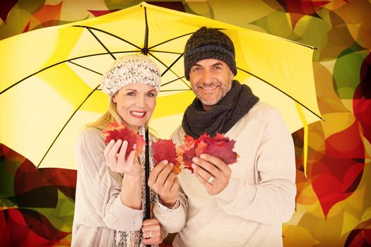 Portrait of couple holding autumn leaves while standing under yellow umbrella against autumnal leaf pattern in warm tones