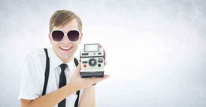 Geeky hipster holding a retro camera against white wall