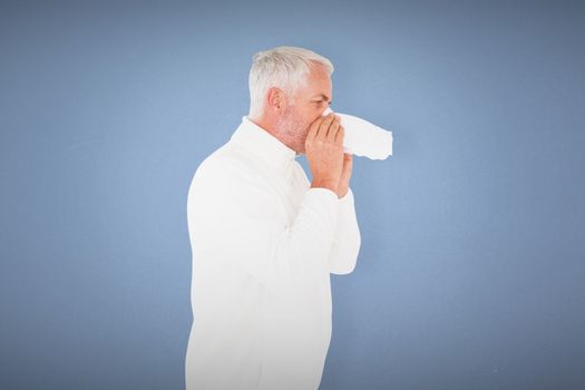 Sick man in winter fashion sneezing against blue background