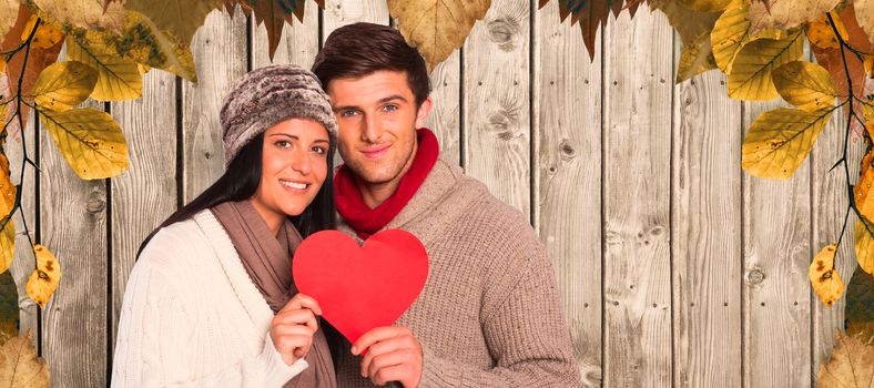 Young couple smiling holding red heart against digitally generated grey wooden planks