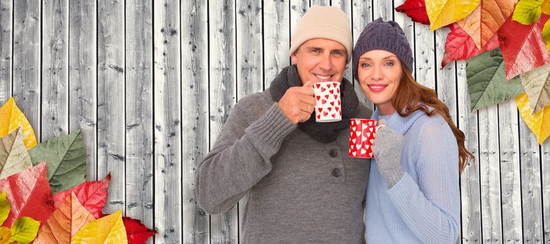 Happy couple in warm clothing holding mugs against digitally generated grey wooden planks