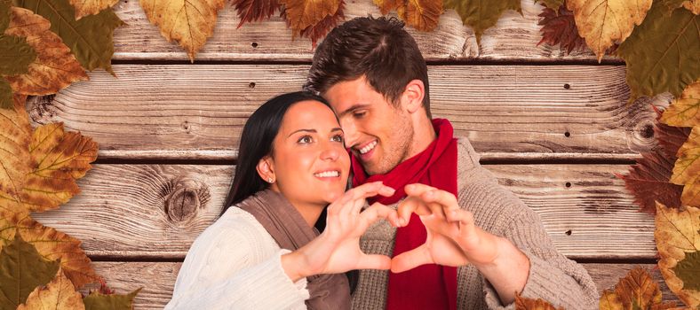 Young couple making heart with hands against wooden planks background