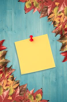 Illustrative image of pushpin on yellow paper  against autumn leaves pattern