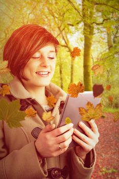 Pretty woman in winter coat using digital tablet against peaceful autumn scene in forest