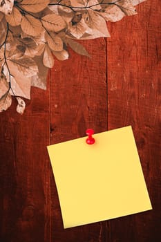 Illustrative image of pushpin on yellow paper  against autumn leaves on wood
