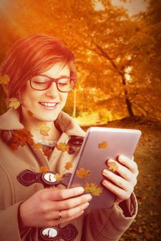 Smiling woman in glasses using digital tablet against autumn scene