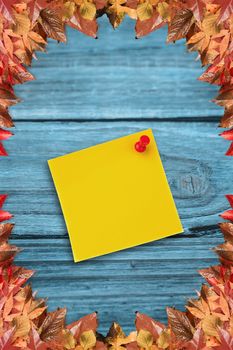 Digital image of pushpin on yellow paper  against autumn leaves pattern