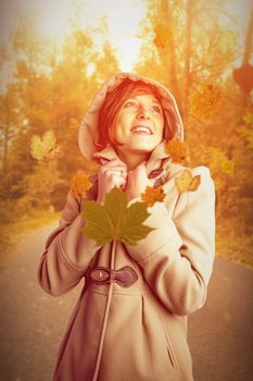 Smiling beautiful woman in winter coat looking up against autumn scene
