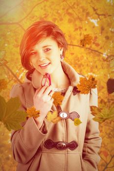 Portrait of pretty woman in winter coat holding glasses against autumn scene