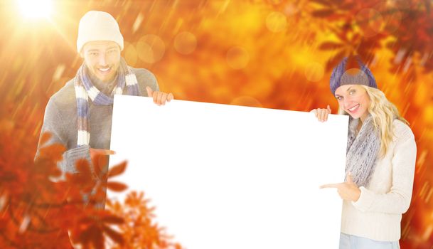 Attractive couple in winter fashion showing poster against autumn scene