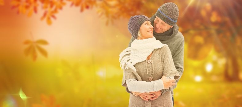 Happy mature couple in winter clothes embracing against autumn scene