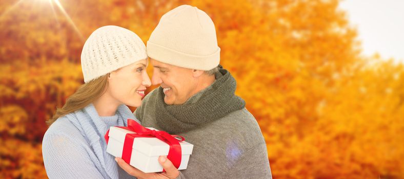 Casual couple in warm clothing holding gift against autumn scene
