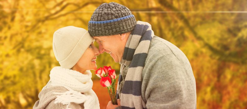 Happy mature couple in winter clothes with roses against peaceful autumn scene in forest