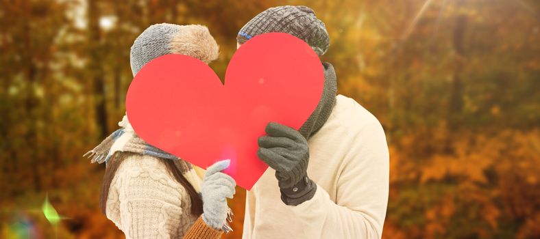 Attractive young couple in warm clothes holding red heart against autumn scene