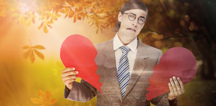 Geeky businessman crying and holding broken heart card against autumn scene