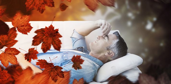 Man suffering from headache while on sofa against autumn scene