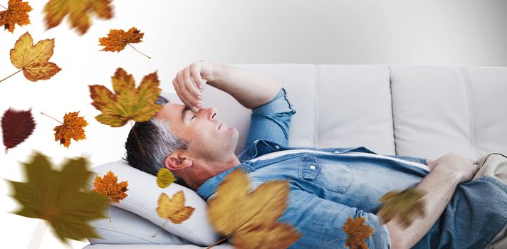 Man suffering from headache while on sofa against autumn leaves