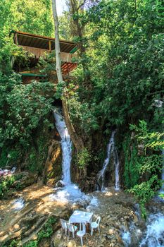 Bottom view of flowing waterfall and observation terrace among trees.