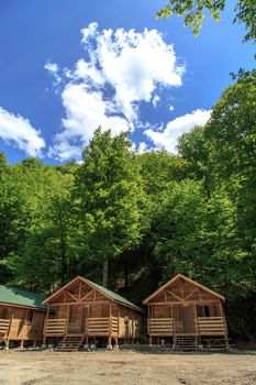 Side view of small wooden bungalows among trees in forest, on blue sky background.