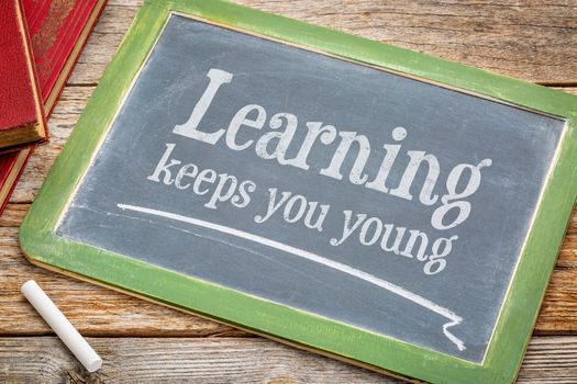 learning keeps you young - inspirationall words with a white chalk on a blackboard with a stack of books against rustic wooden table