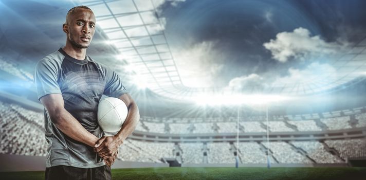 Portrait of confident sportsman with rugby ball against rugby stadium