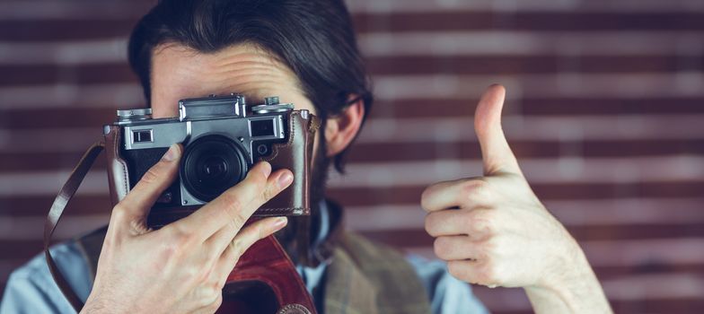 Man showing thumbs up gesture while photographing against brick wall