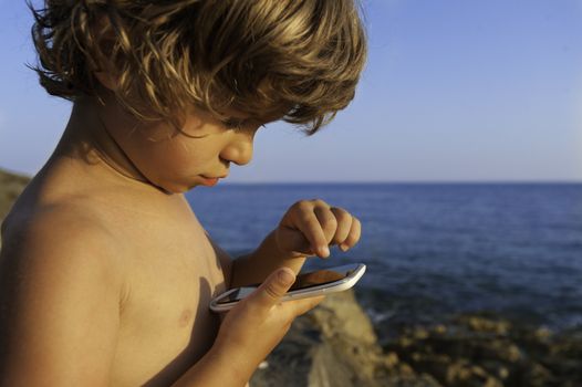 Little boy playing with a smartphone on the beach. Modern lifestyle, modern generation concept.