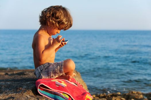 Little boy playing with a smartphone on the beach. Modern lifestyle, modern generation concept.