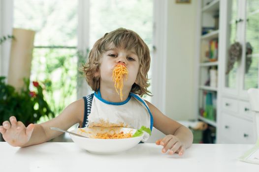 Portrait of a cute young boy making a mess while eating pasta for lunch. Band manners.