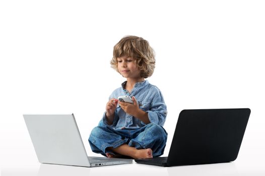 Little boy happy enjoying modern generation technologies playing indoors using two laptops and smart phone