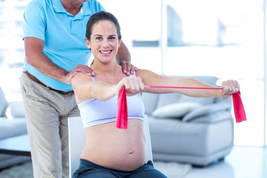 Portrait of smiling pregnant woman stretching exercise band while therapist massaging 
