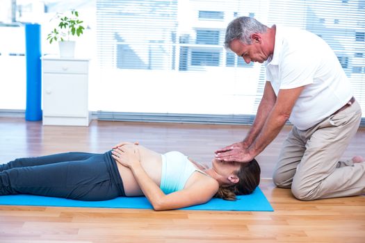 Therapist performing reiki on young pregnant woman 