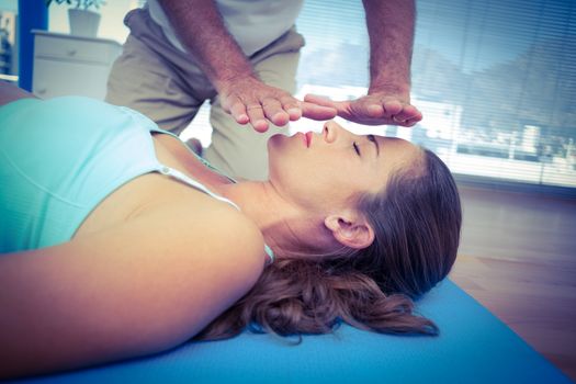 Therapist performing reiki on young woman in health club