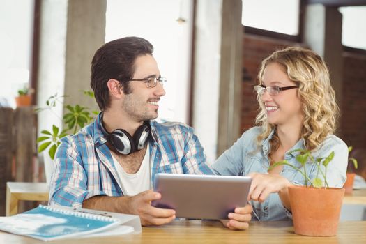 Happy business people discussing while holding digital table in creative office