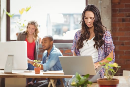 Businesswoman using laptop while colleague seen in background at creative office