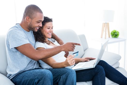 Couple enjoying online shopping sitting on sofa at home