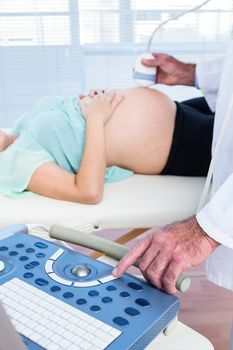 Midsection of male doctor performing ultrasound test on pregnant woman in hospital