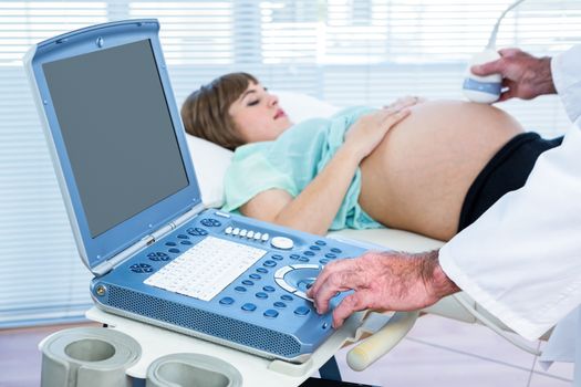 Pregnant woman lying while doctor performing ultrasound test in clinic