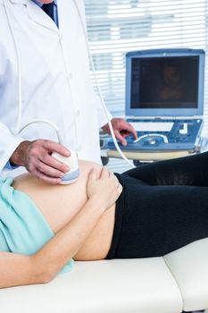 Midsection of doctor performing ultrasound on pregnant woman in clinic