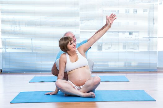 Instructor teaching yoga to pregnant woman in class