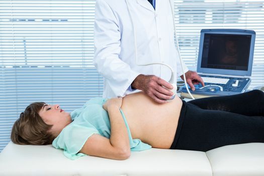 Midsection of male doctor performing ultrasound on pregnant woman