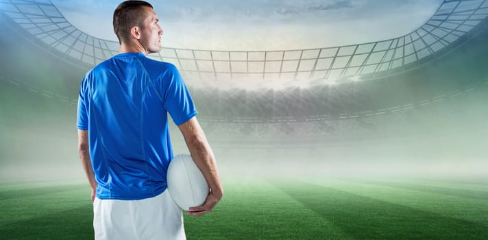 Rugby player looking away while holding ball against rugby stadium