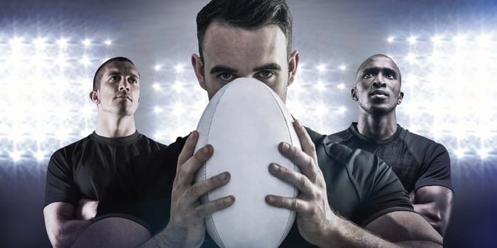 Tough rugby player holding ball against spotlight