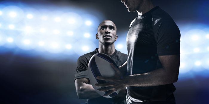 Calm rugby player thinking while holding ball against spotlights